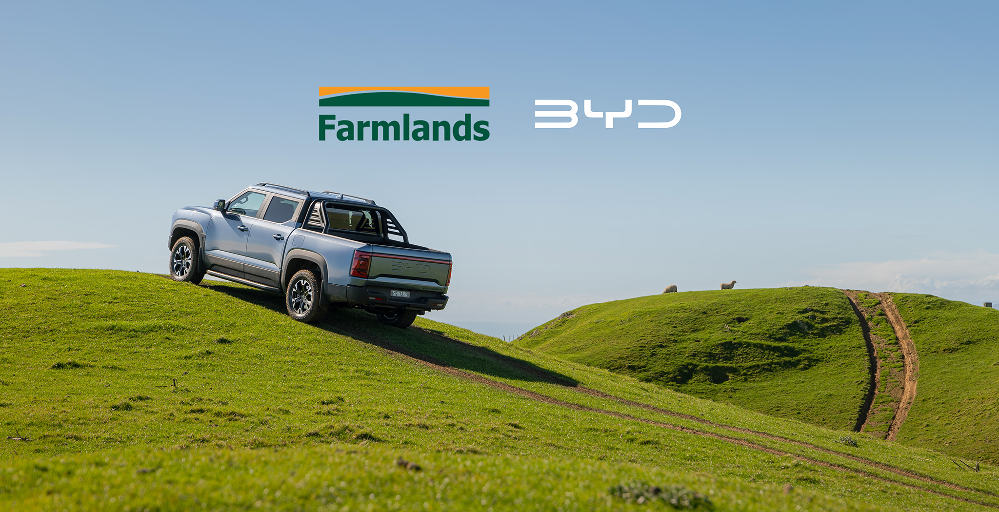 BYD Shark 6 parked on grass hill with Farmlands and BYD logo above