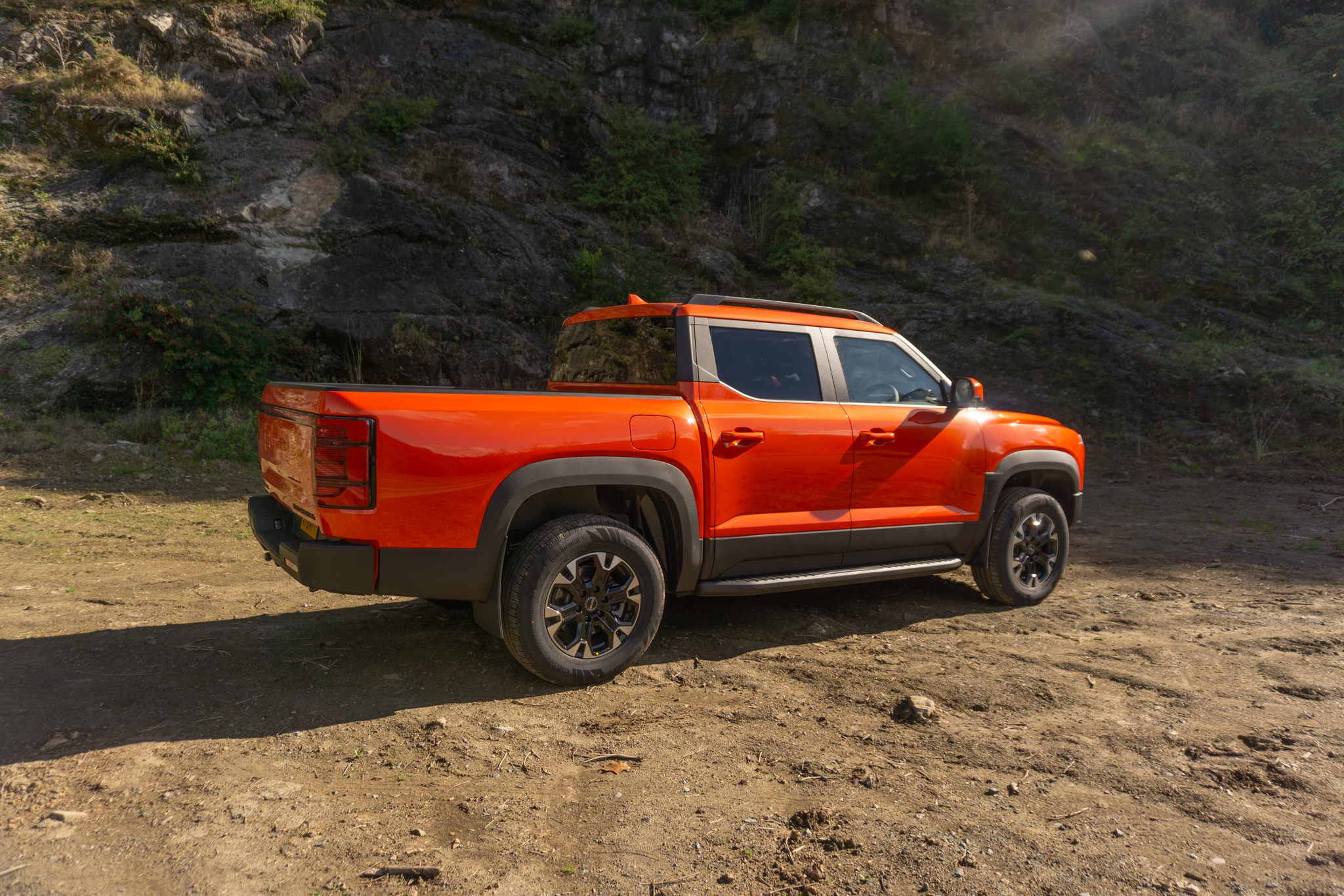 BYD Shark 6 Orange, rear 45 degree angle shot in front of rock wall