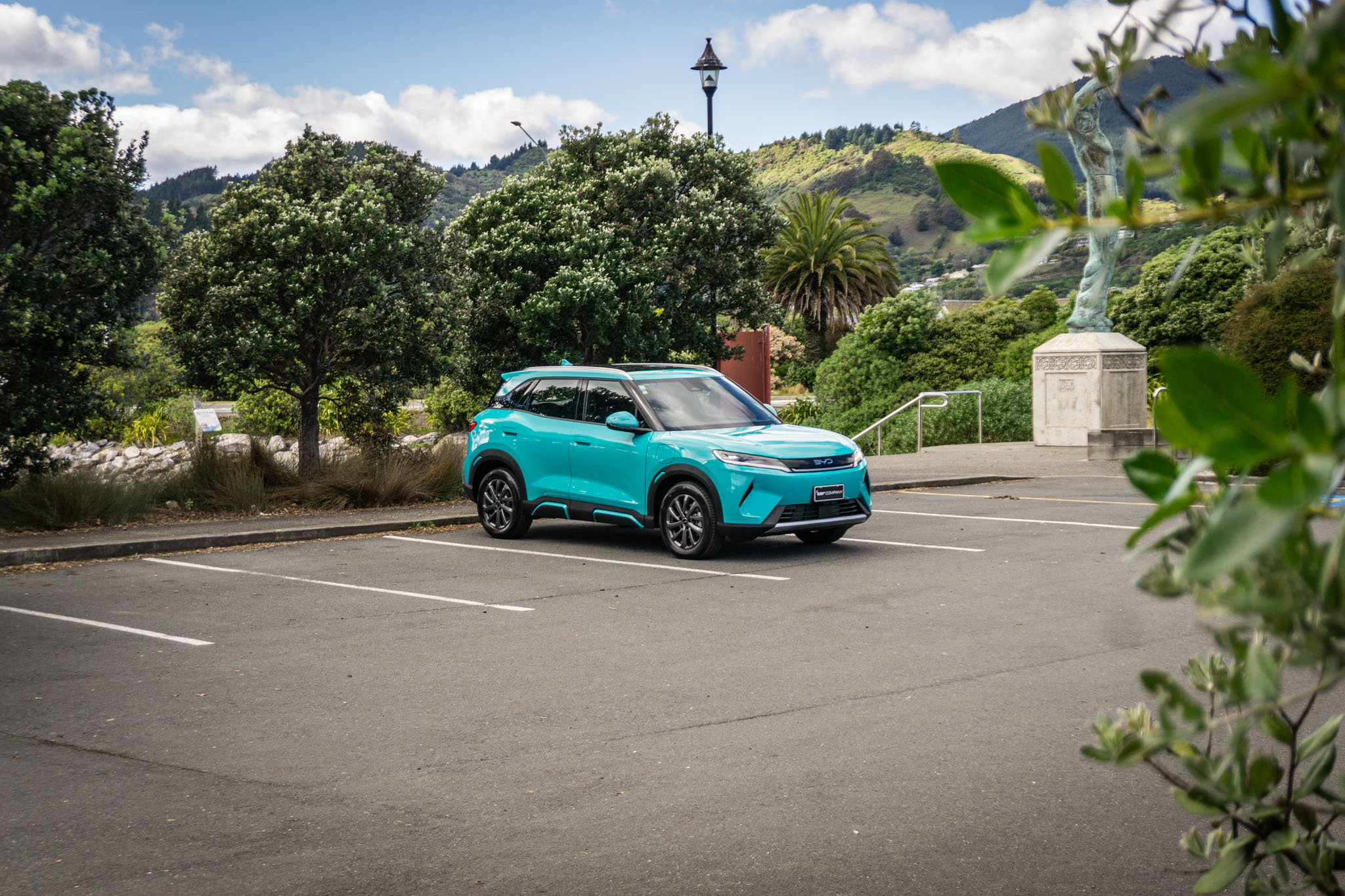 BYD Atto 2 DM-i Super Hybrid in Turquoise paint, parked in Nelson car park with bushes and trees behind